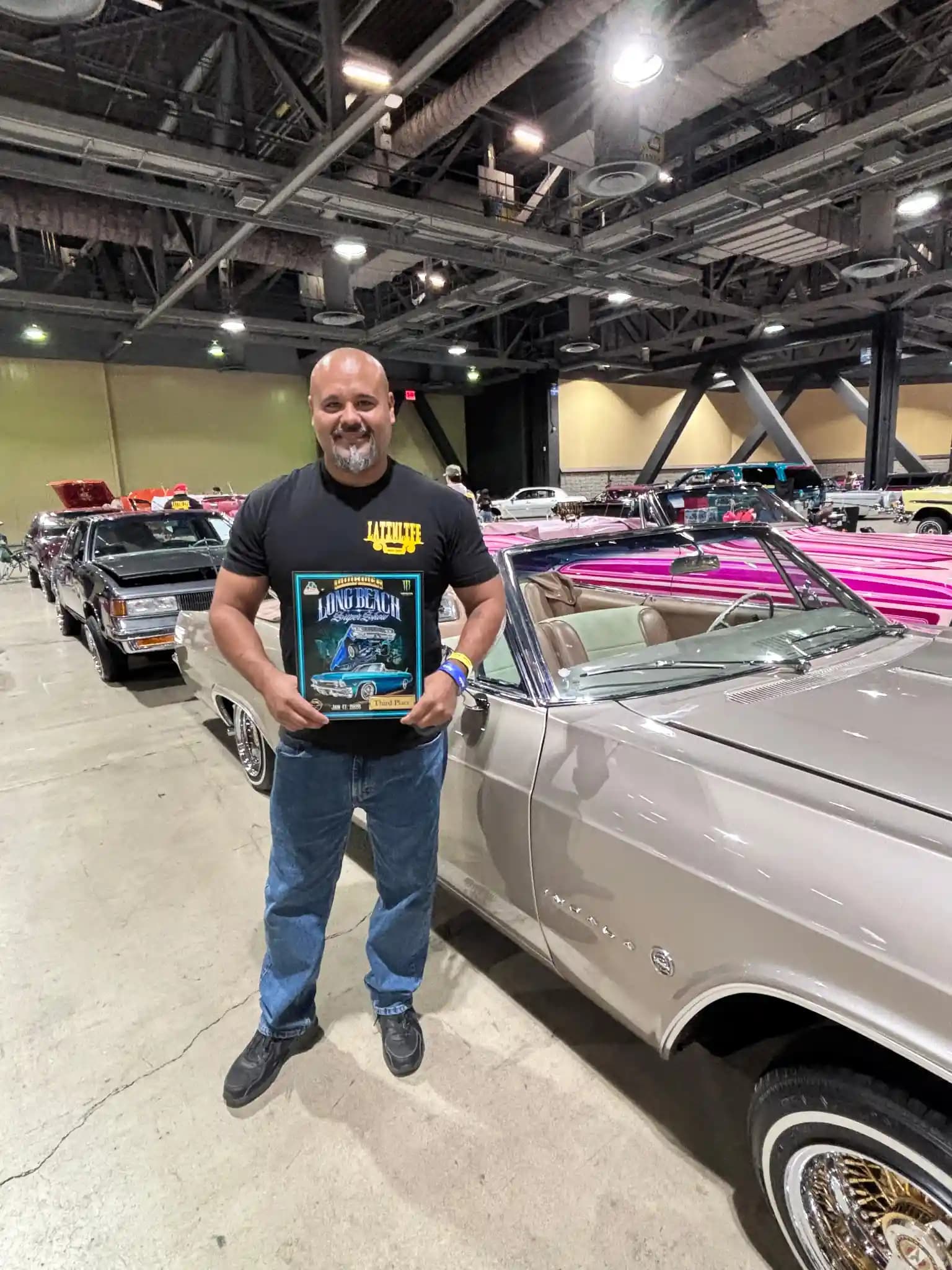 Customer holding a Third Place award in front of his lowrider at the Long Beach Lowrider Super Show